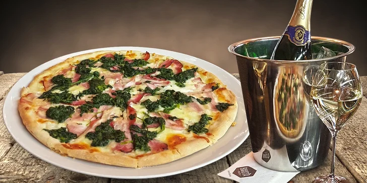 Dvě bohatě zdobené pizzy a lahev sektu v kavárně plné umění