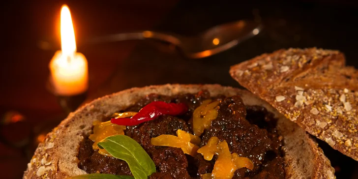 Pikantní guláš v chlebu sypaný cheddarem v restauraci plné pivních speciálů