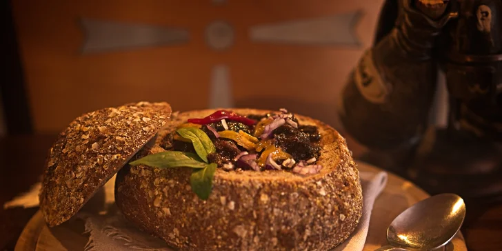 Pikantní guláš v chlebu sypaný cheddarem v restauraci plné pivních speciálů