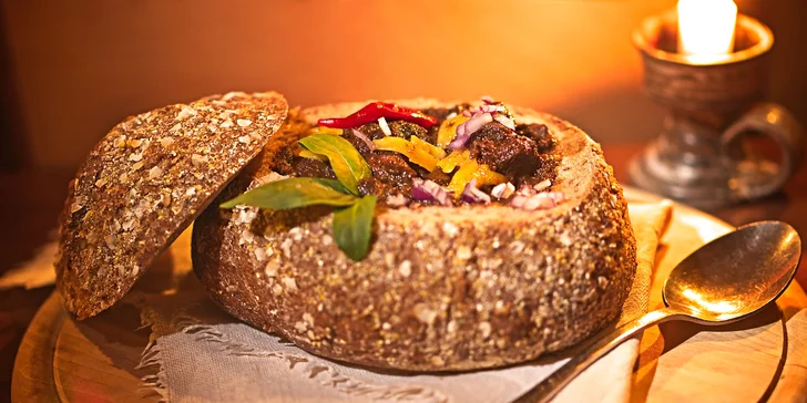 Pikantní guláš v chlebu sypaný cheddarem v restauraci plné pivních speciálů